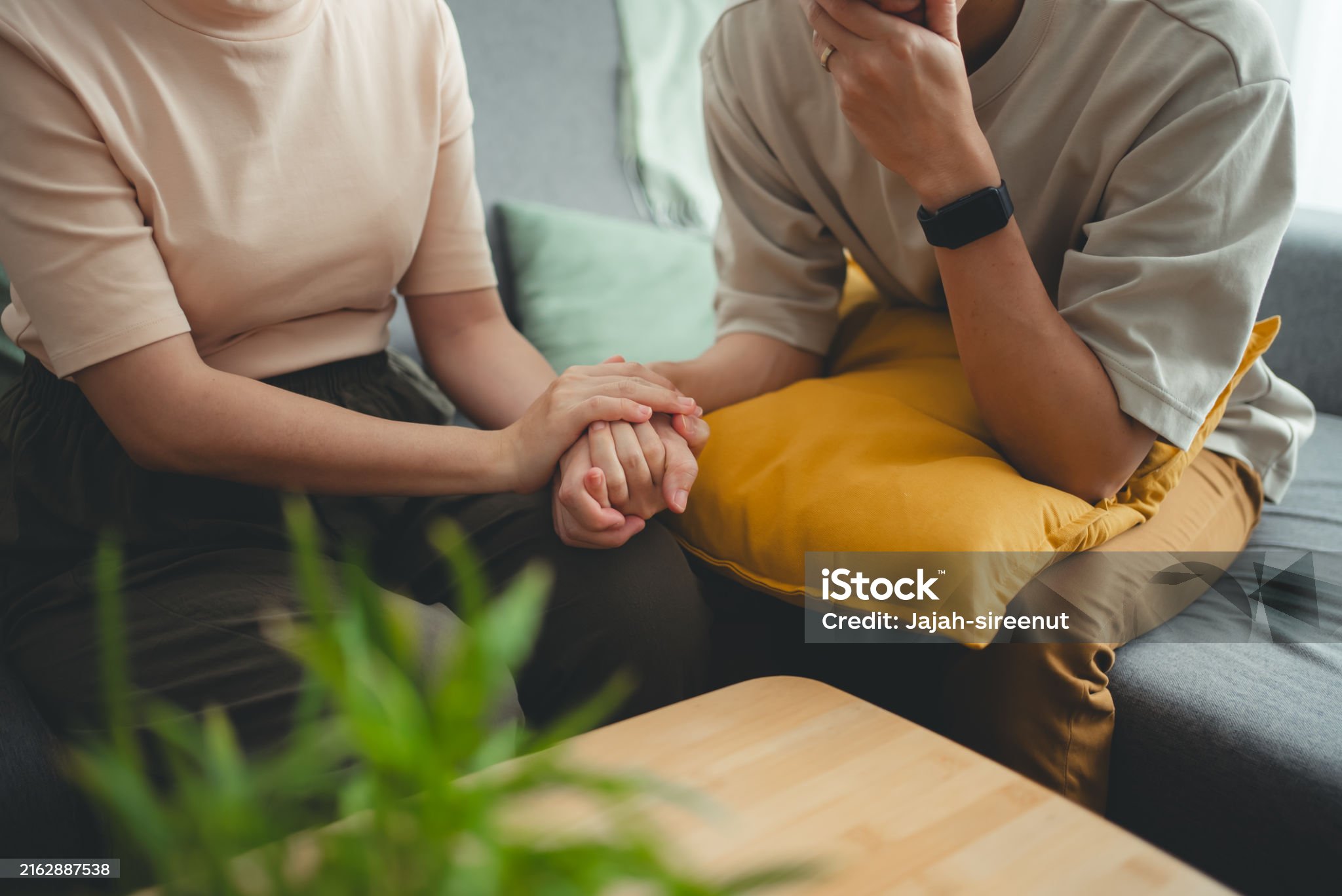 Close up shot of couple holding hands sharing love and care together sitting in living room at home.